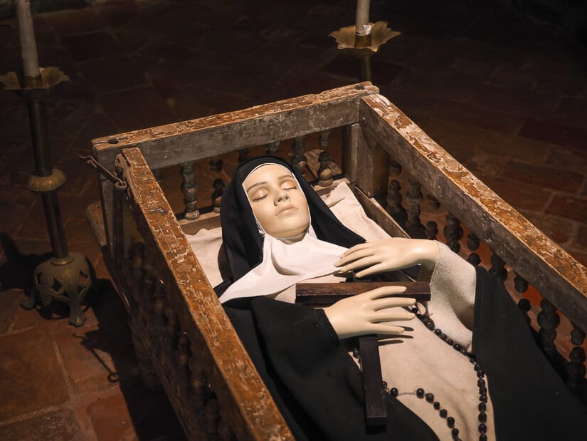 A nun statue lying down holding a cross in a wooden bed