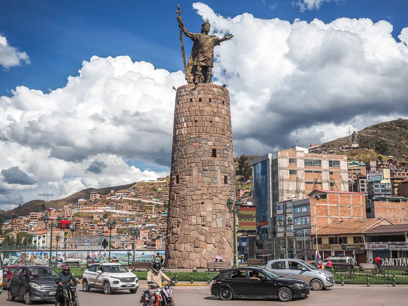 A tall stone tower with statue of Pachacutec on top, with traffic driving around it