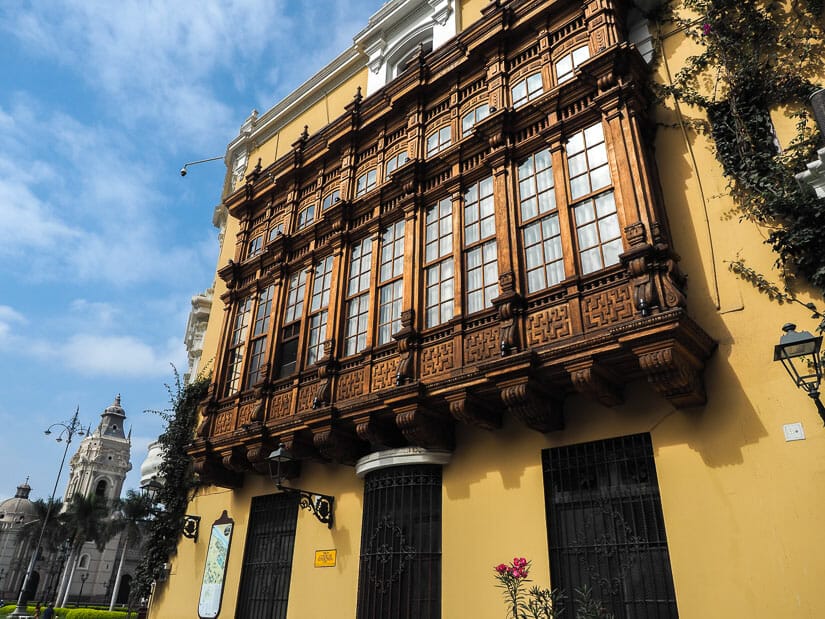 Yellow side wall of the Municipal Palace, with beautiful wooden window frames sticking out, and Lima Cathedral in background