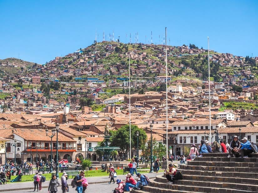People sitting on the stairs in front of the Plaza de Armas in Cusco, with hills covered in houses in background