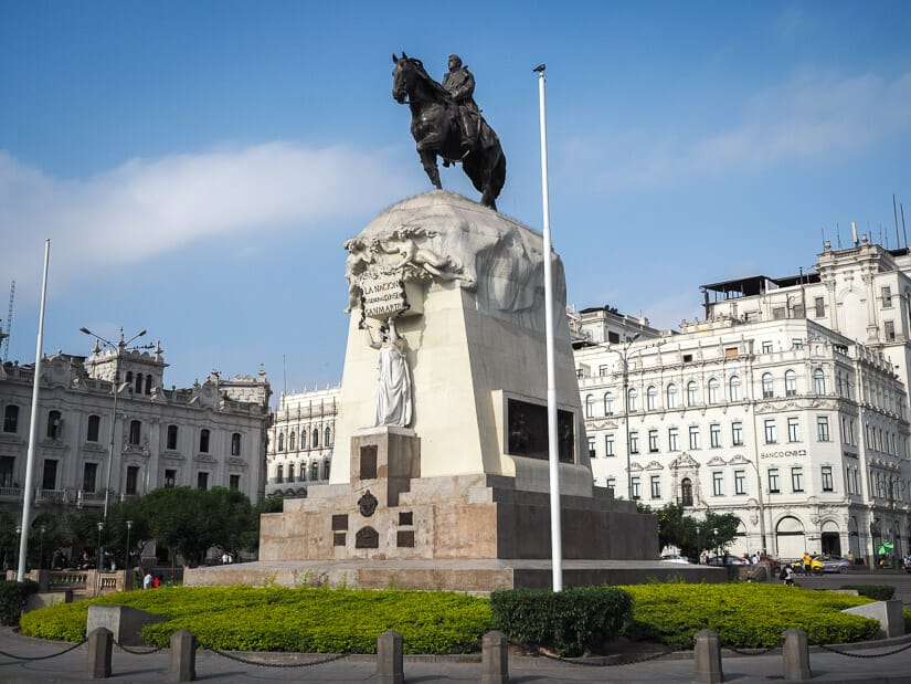 A huge monument with statue of man riding a horse on top, in a square, with white neoclassical buildings behind