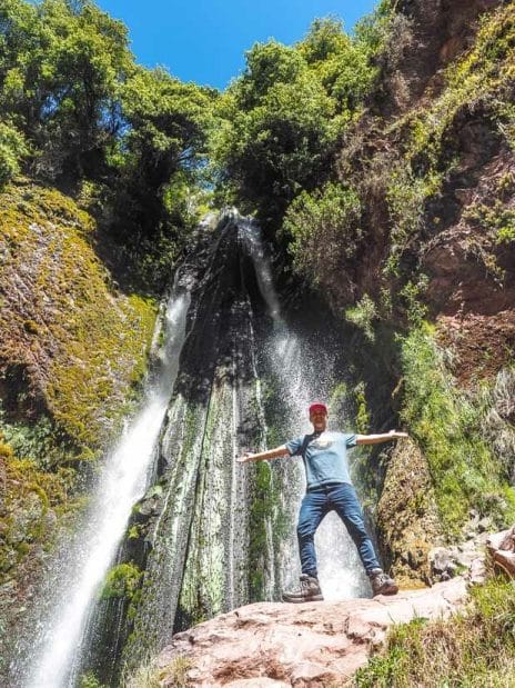 Nick Kembel standing in front of a Poc Poc Waterfall with his arms outstretched 
