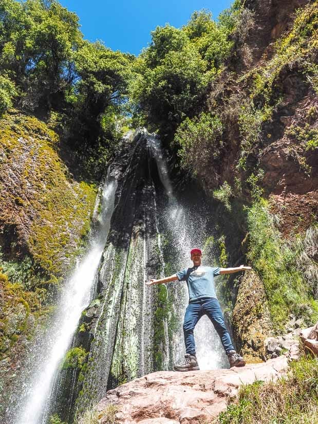 Nick Kembel standing in front of a Poc Poc Waterfall with his arms outstretched 