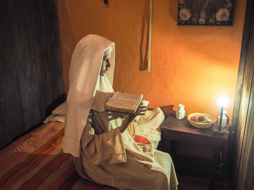 Statue of a nun sitting on a bed, holding a book, and praying