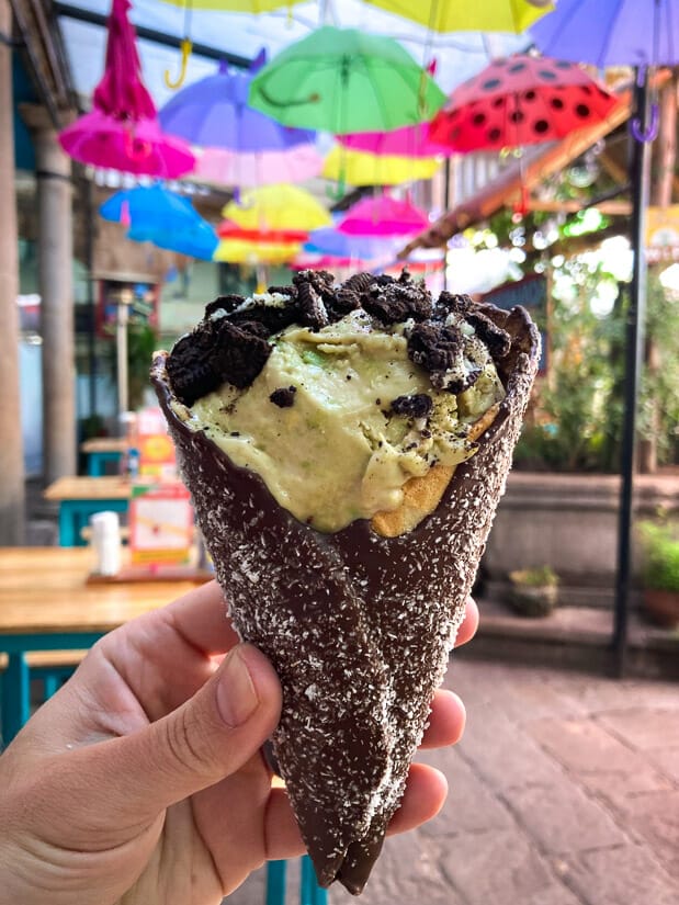 A hand holding up a fancy ice cream cone with colorful umbrellas hanging from ceiling