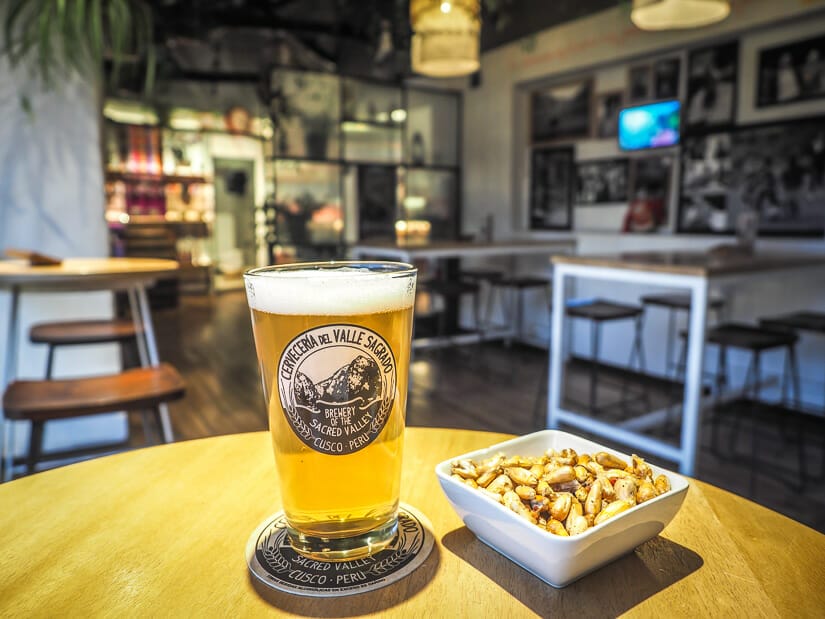 A pint of beer in a Sacred Valley Brewery glass on a table in a pub with a bowl of fried corn kernels