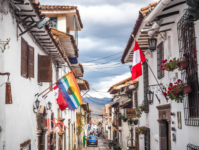 A typical lane in San Blas with white buildings on either side and a rainbow Inca flag and red and white Peru flag