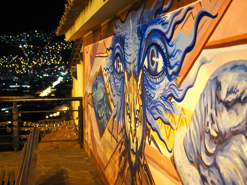 A street art mural of a cat with a view of the lights of Cusco at night