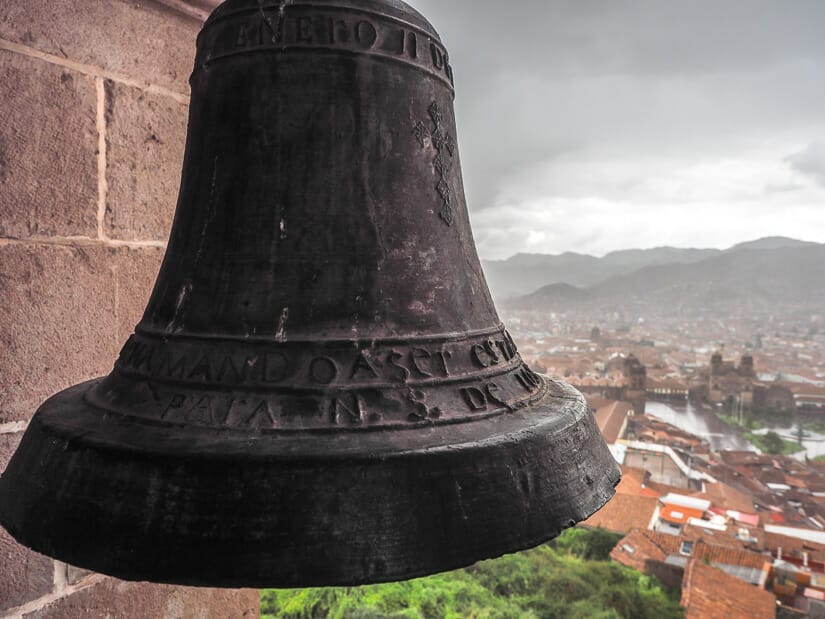 A large metal bell hanging in a bell tower overlooking Cusco