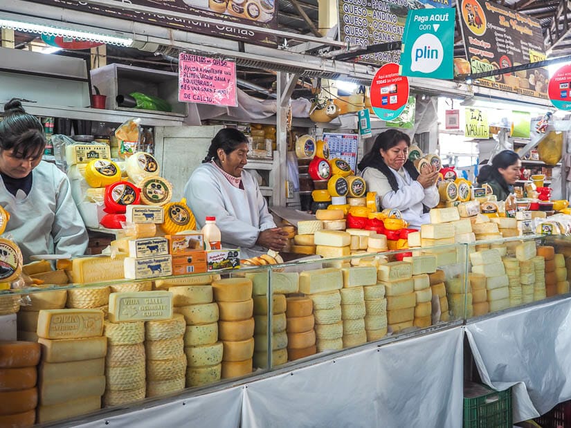 Three female vendors behind huge stacks of cheese in a traditional market