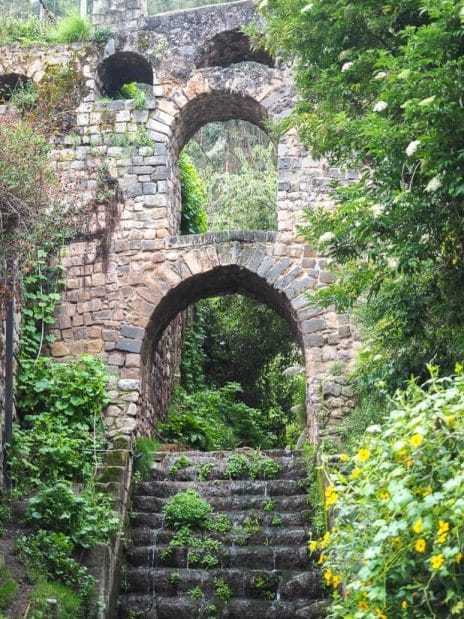 Looking up at a stone arch aqueduct with water flowing stairs below it