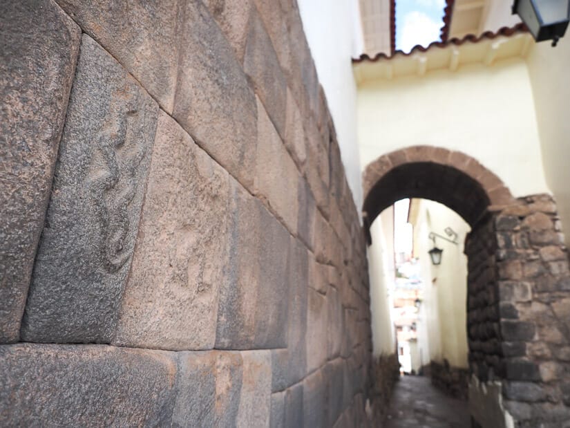 An Inca stone wall on the left with some snake patterns and an arched alleyway