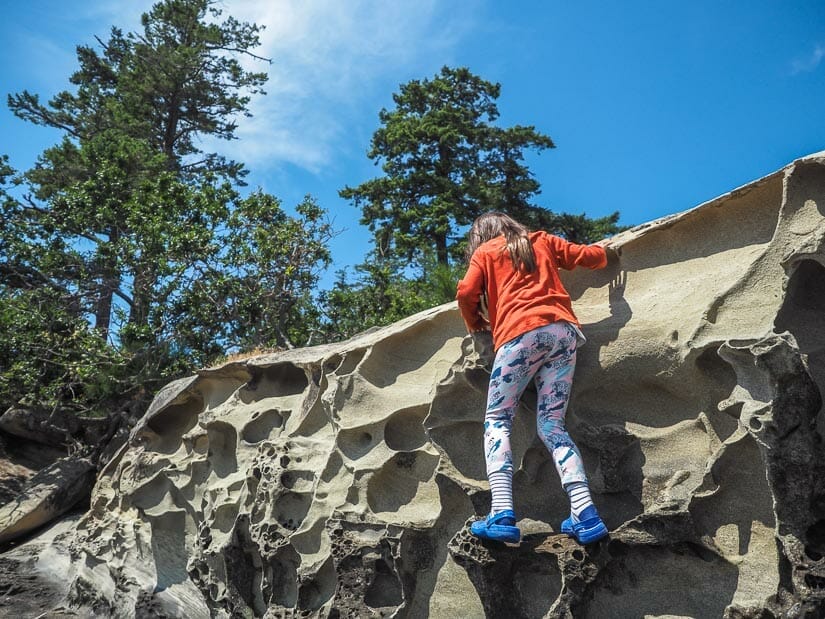 A young girl climbing a sandstone cliff with holes in it