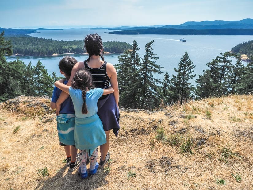 A woman and two kids from behind, as they face the view of a ferry passing between two islands