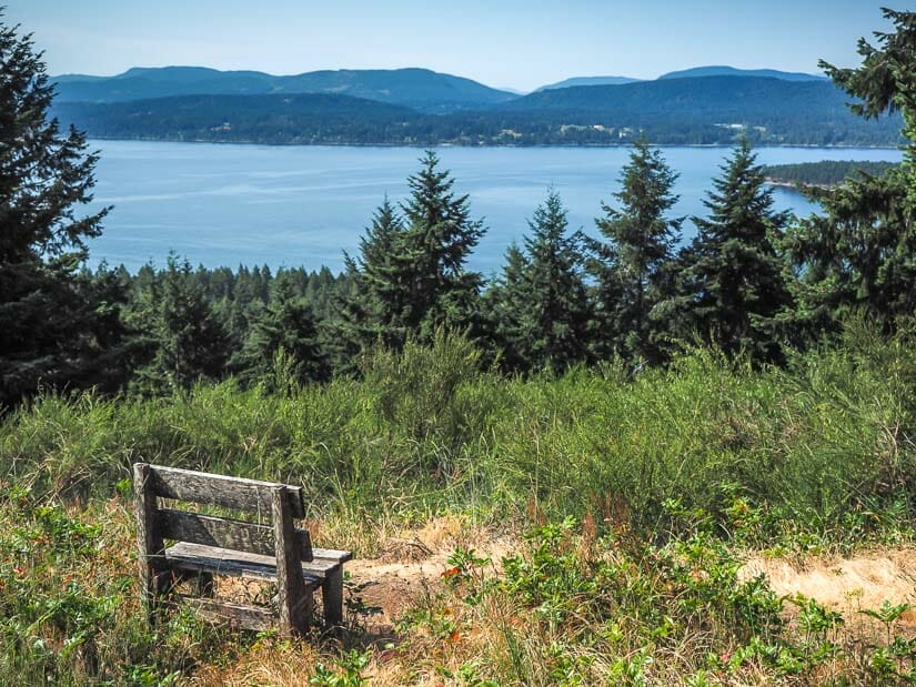 A bench on top of a hill, with view of forest below, sea, and islands in the distance