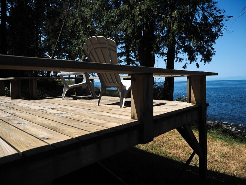 A wooden balcony with two chairs facing the ocean