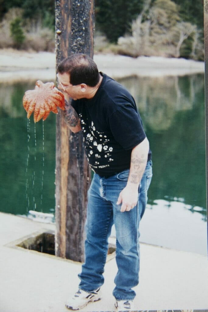 A man holding up an orange sea star with many legs and pretending to eat it