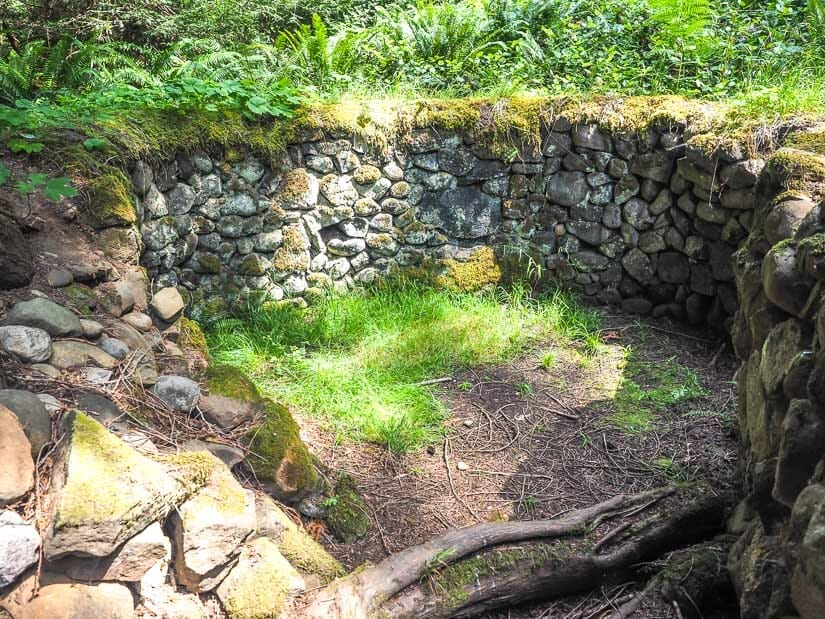 A round stone pit kiln in the ground built of stones with tree beside