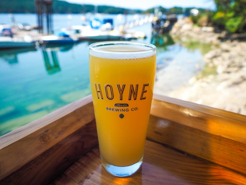 A pint of hazy beer on the corner of a wood bar, with a view of a harbor in the background