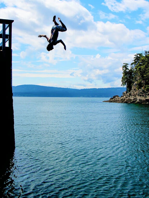 Nick Kembel doing a back flip off a tall dock, completely upside down in the air