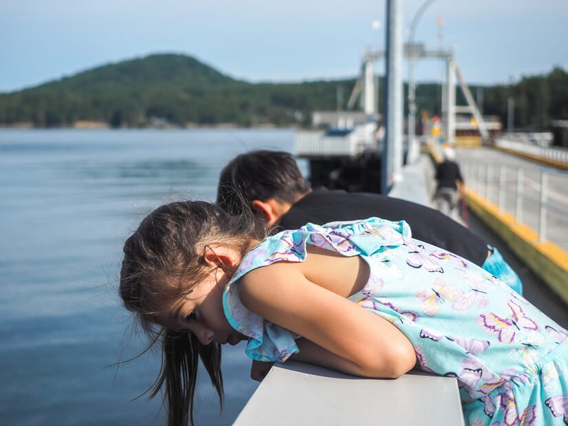 Two kids leaning over the side of the dock at a ferry terminal 