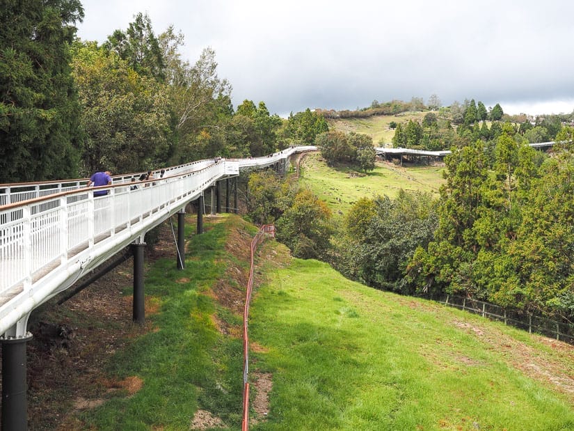 A long white walkway on the left goes uphill above some grassy fields