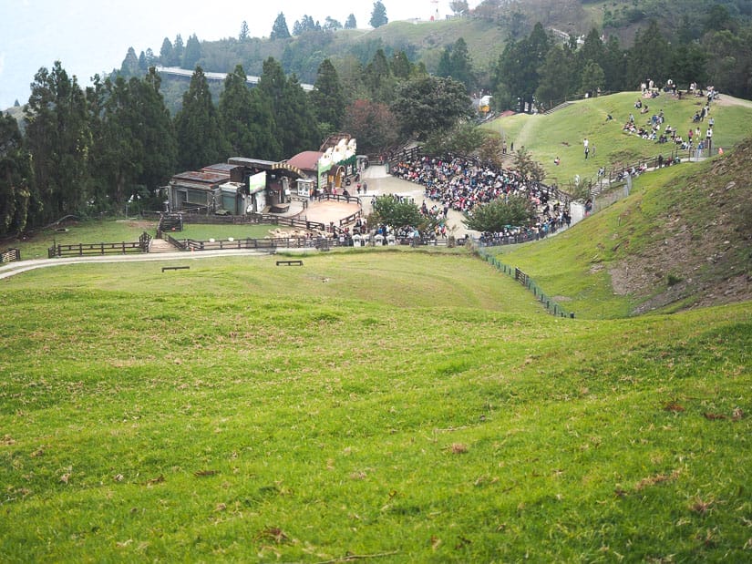Looking down some grass-covered hills at a small stage with many people sitting around it
