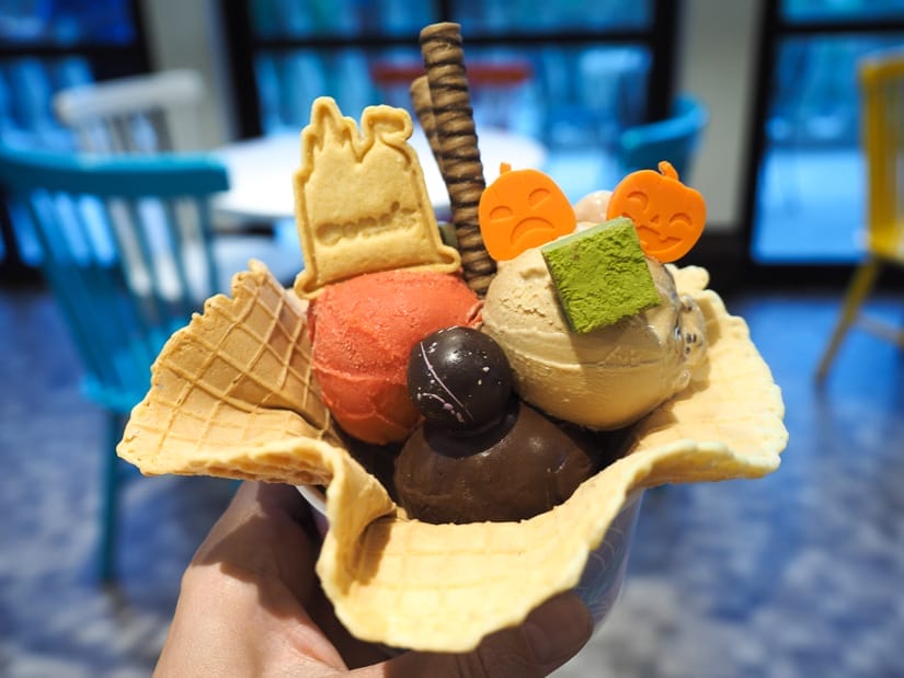 A hand holding up a waffle cone cup filled with scoops of ice cream, chocolates, and cookies