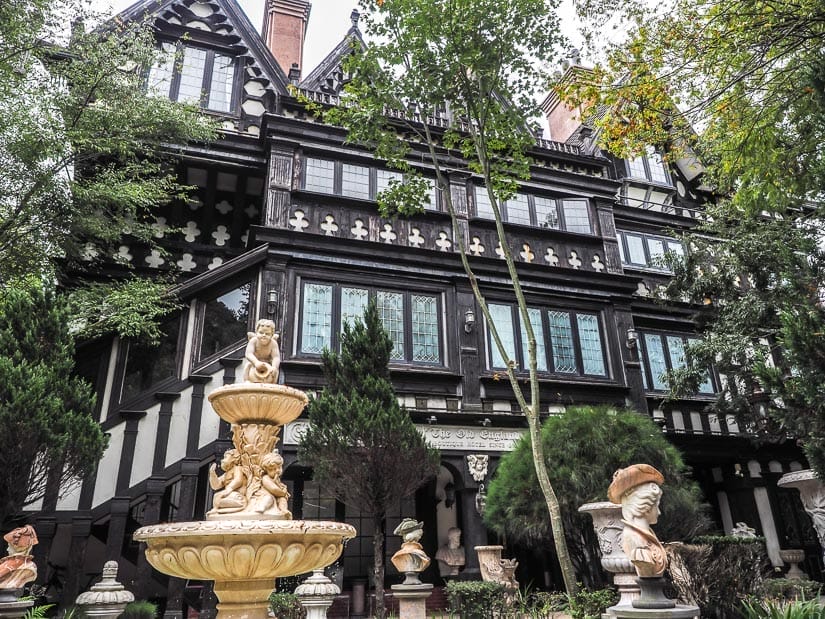 The side of a castle-like hotel with fountains and sculptures in the yard at the bottom