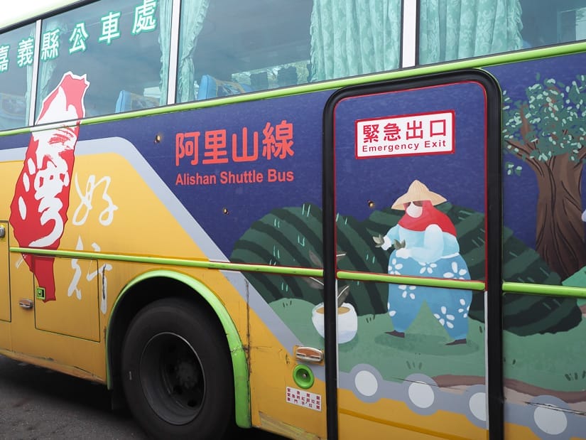 Close up of the side of an Alishan shuttle bus, which is purple and yellow with designs of a tea farmer on the side