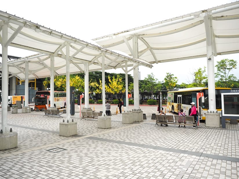 A large, open, outdoor bus station with a couple buses parked at it