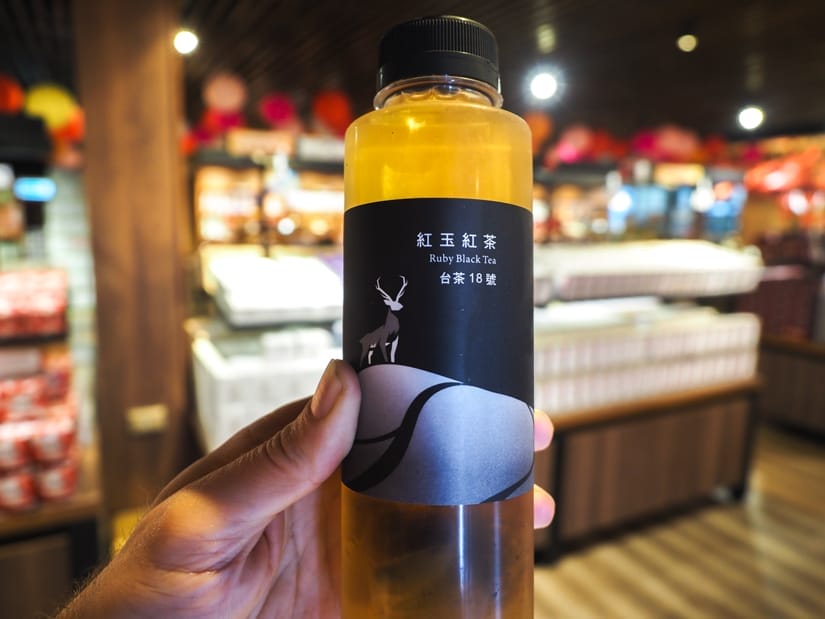A hand holding a bottle of iced Ruby Red black tea inside a gift shop at Hohocha