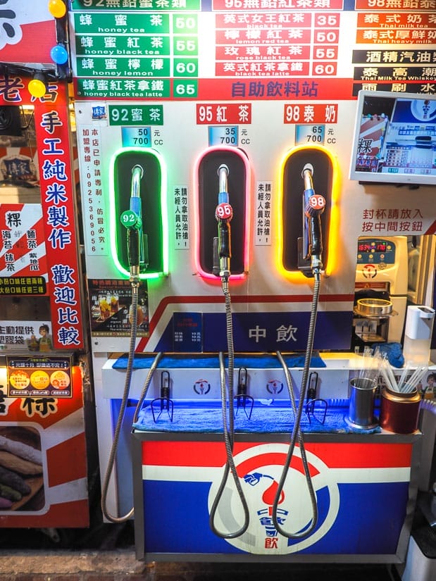 A night market stall designed to look like the gas pump at a Taiwanese gas station, with three dispensers for three different kinds of iced tea, each lit up with a yellow, red or green light, and a menu showing the drink types