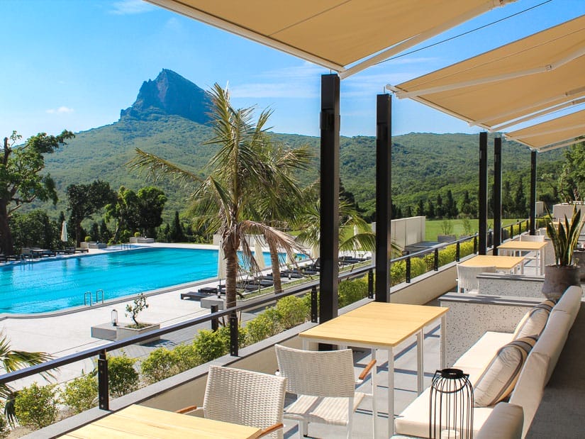 Looking out from a hotel patio with chairs and tables out at a pool and a mountain peak beyond