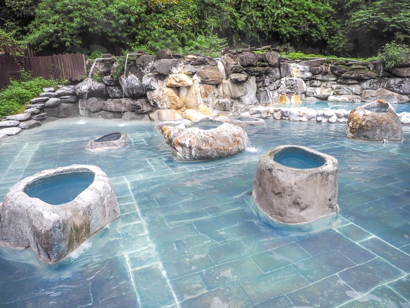An outdoor thermal hot spring pool with shallow water and some raised, round, individual bathing tubs