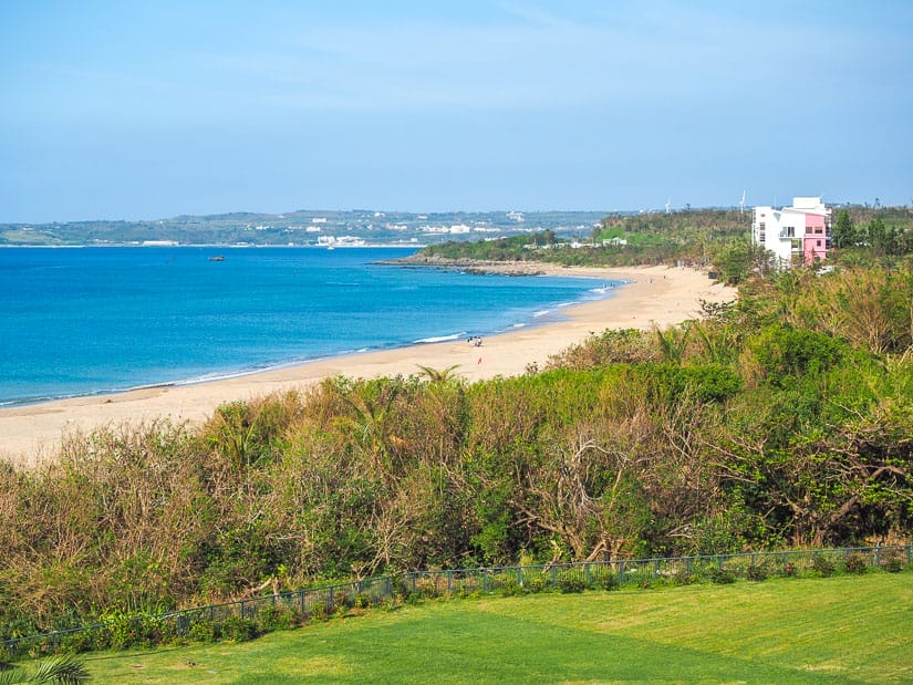 Looking down a long stretch of beach with no one on it and trees and grass in the foreground