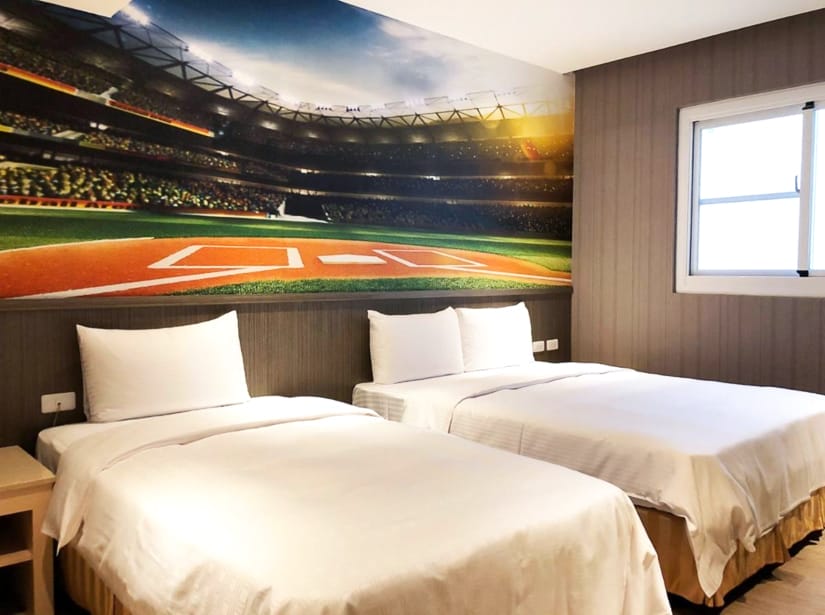 Two beds in a hotel room with a picture of a baseball diamond on the wall above