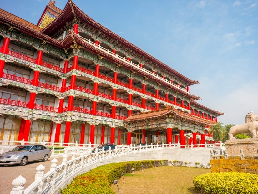 A classic Chinese style hotel with red columns and a car parked on the driveway in front