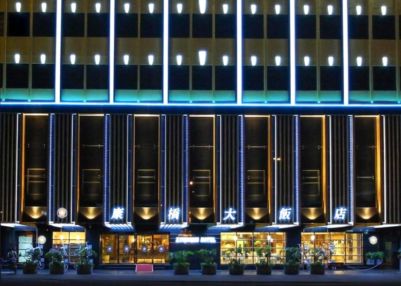The exterior of a hotel shot at night, with bright lobby at the bottom and dark room windows above