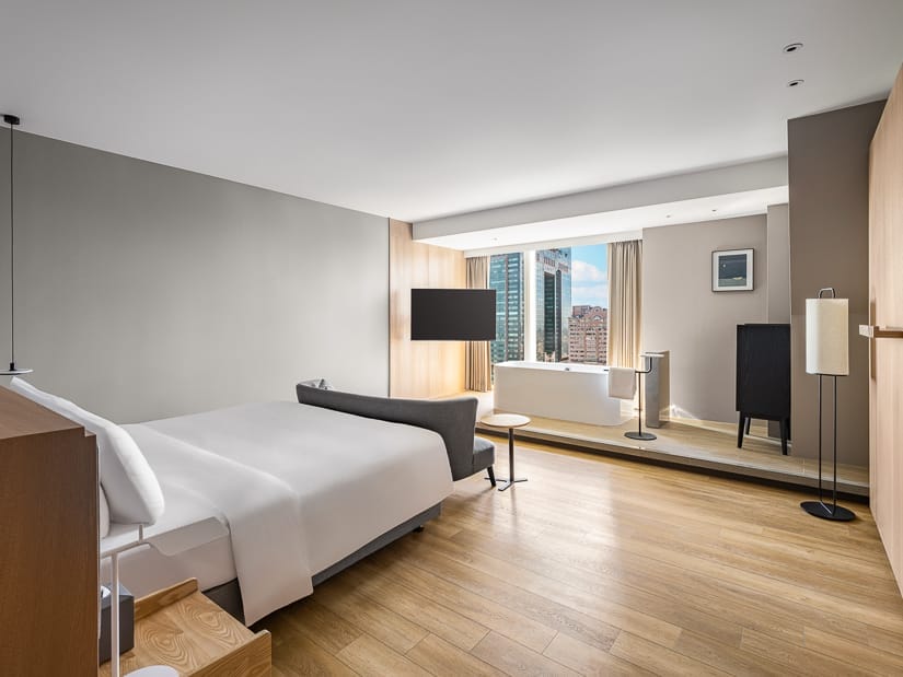 A hotel room viewed from its door, with a white bed and a bath tub by the window