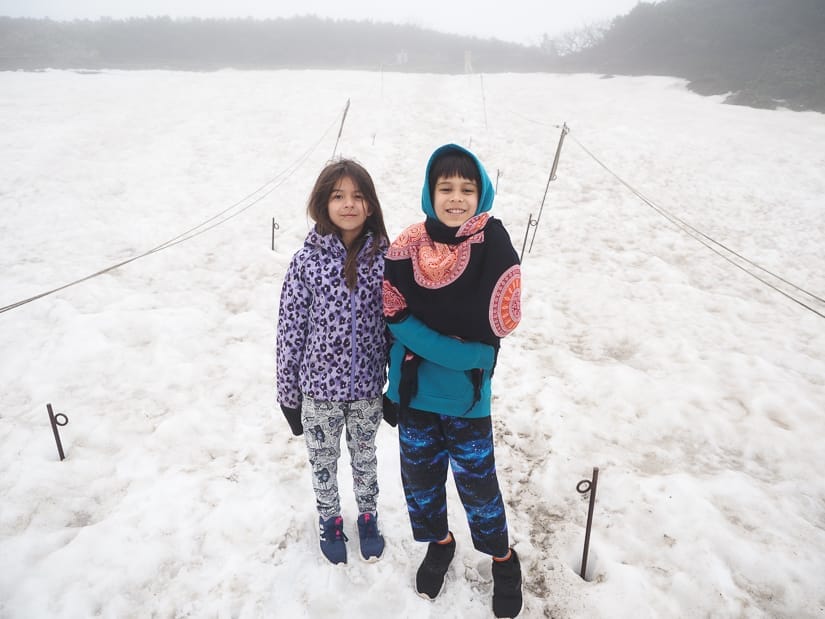 Two kids standing on a snow covered trail demarcated with ropes on either side