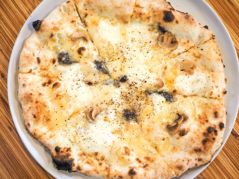 Looking straight down at a wood fired cheese and mushroom pizza cut into slices
