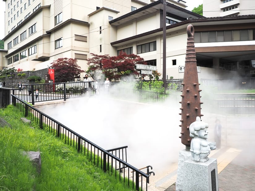 A passageway with steam pouring out from it in a plaza in front of a large hot spring resort