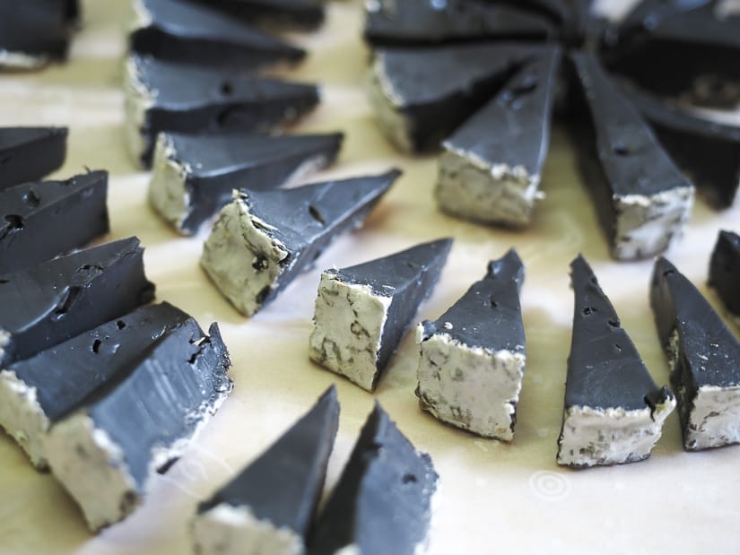 Close up of around a dozen pyramid shaped samples of black cheese