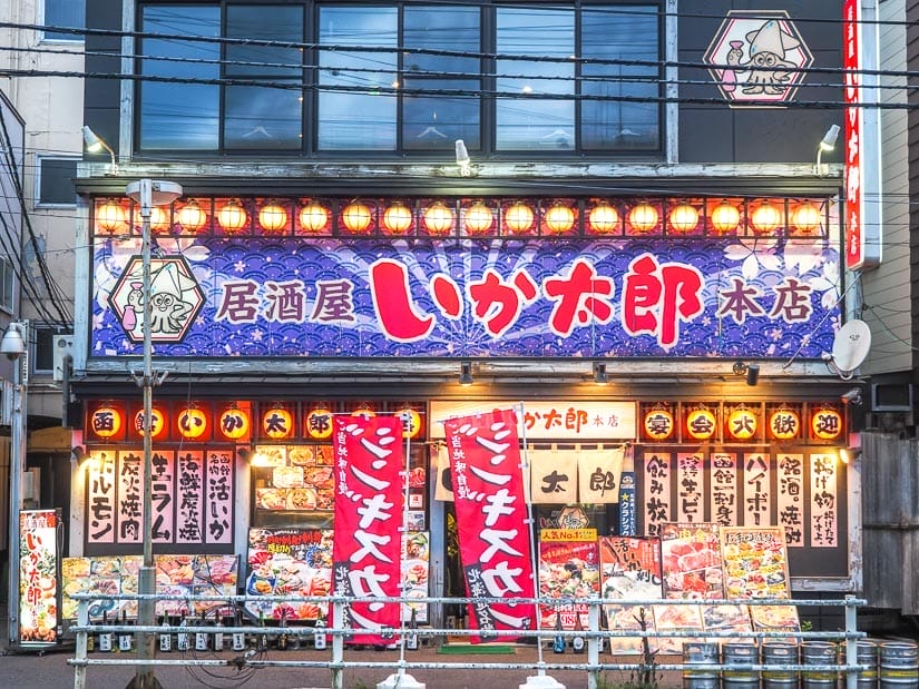 The exterior of a restaurant in Hakodate, Japan, with tons of decorations, lights, and hanging signs with menu items written in Japanese on them