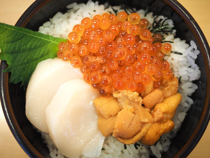 Looking straight down at a bowl of raw scallops, fish eggs and sea urchin on rice