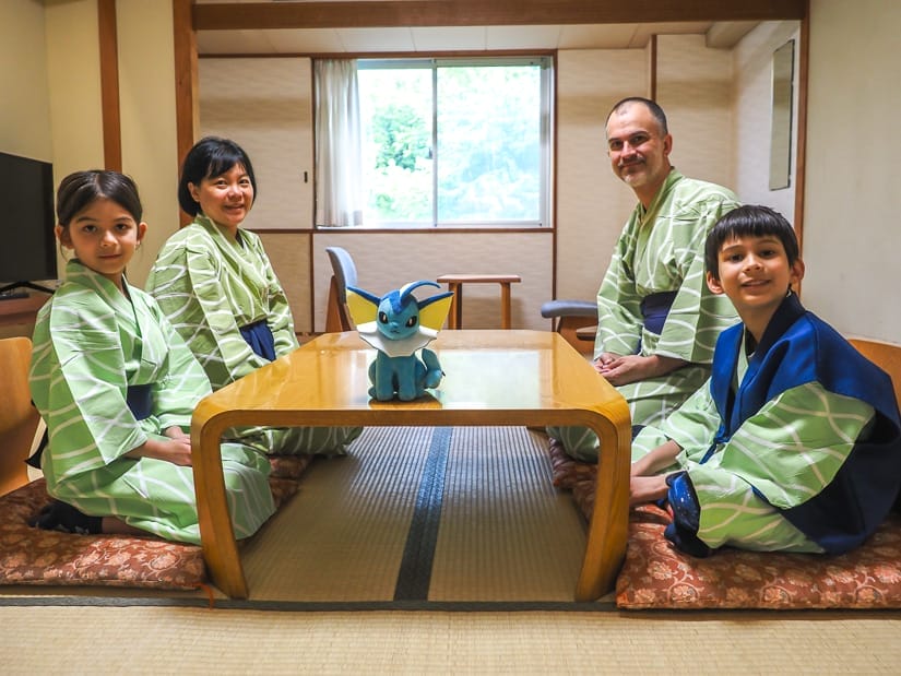 Nick Kembel, his wife, and two kids dressed in traditional green yukatas kneeling at a low table in a Japanese-style tatami hotel room, with a blue pokemon stuffie on the table