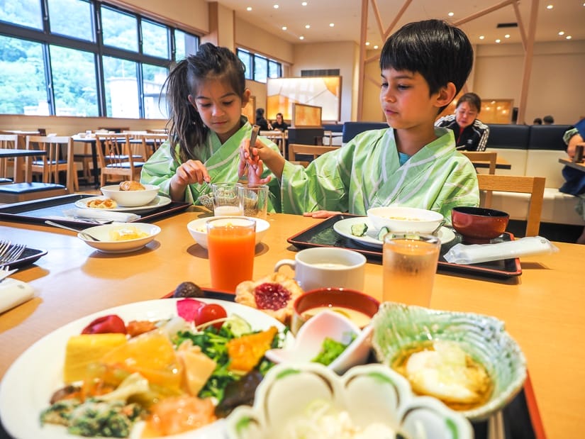 Two kids in traditional Japanese robes sitting at a wooden table, with a huge plate of food in the foreground