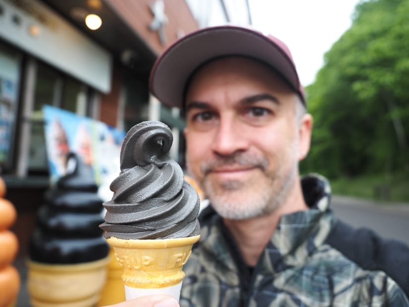 Nick Kembel holding up a black soft serve ice cream cone with ice cream in focus and his face a little blurred behind it