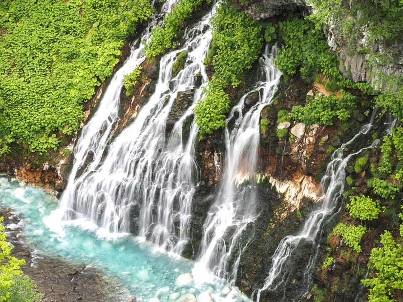 A wide waterfall shot in a way that it's blurred, plunging down a cliff into a bright blue river